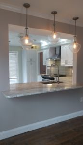 A kitchen counter that extends into another room with three hanging lights above it.