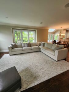 A remodeled living room with a carpet and a kitchen in the background.